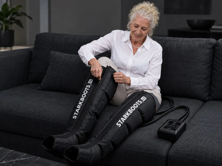 Ältere Frau legt STARKBOOTS V2 auf dem Sofa an und schließt den Reißverschluss.