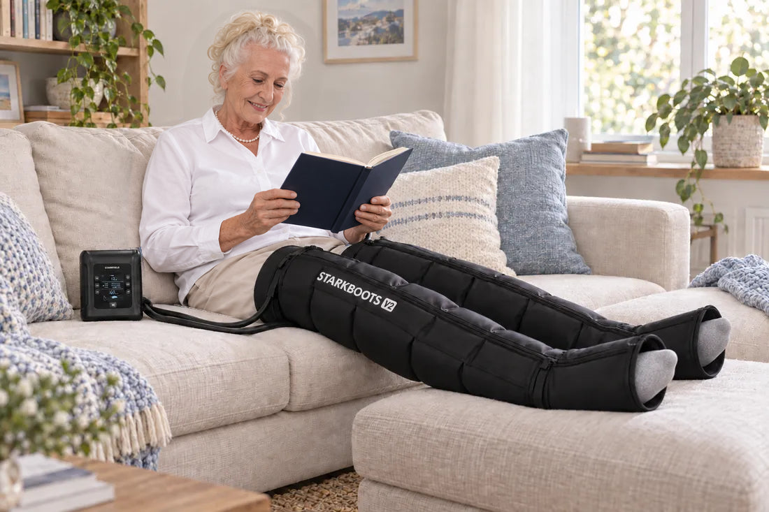 Ältere Frau liest auf dem Sofa mit STARKBOOTS V2 und bequem abgelegten Beinen.